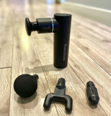 massage gun from StudioHealth Vancouver displayed with various interchangeable heads, used for muscle recovery, deep tissue massage, and pain relief